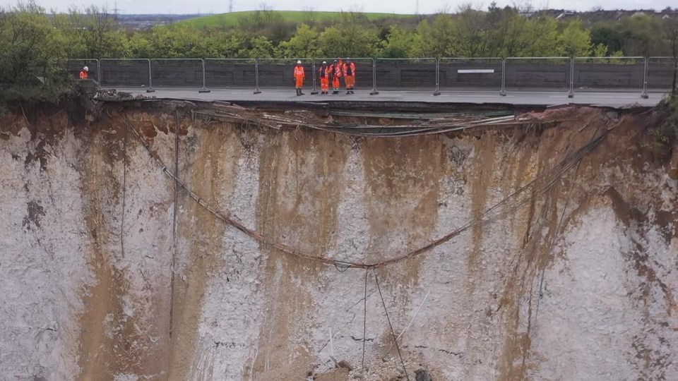 Workers inspecting a large landslip on a road.