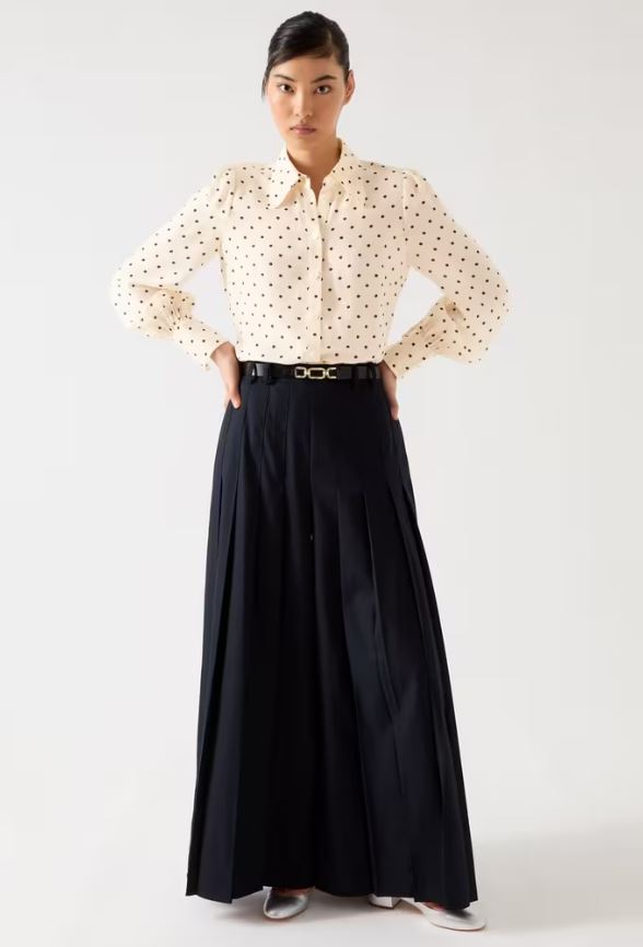 Woman wearing a cream polka dot shirt and wide-leg black pants.