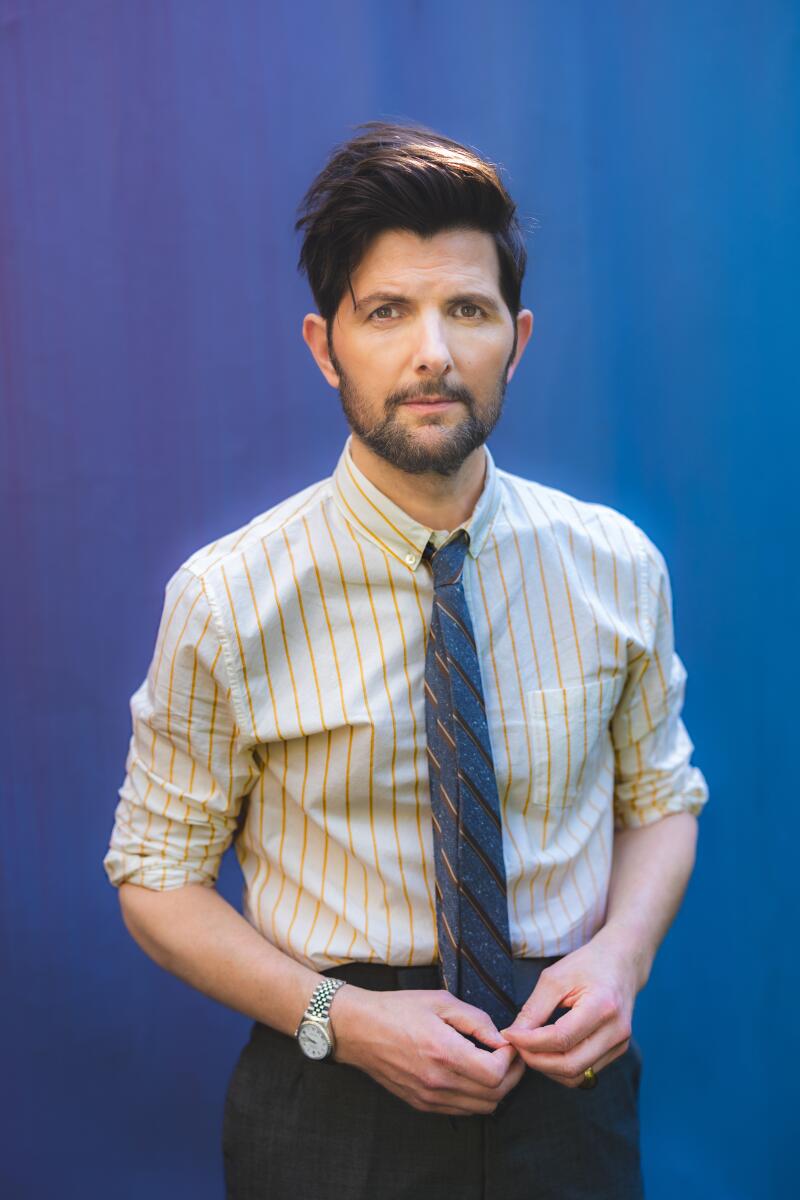 A man in a striped shirt and blue tie with his hands near his waist.