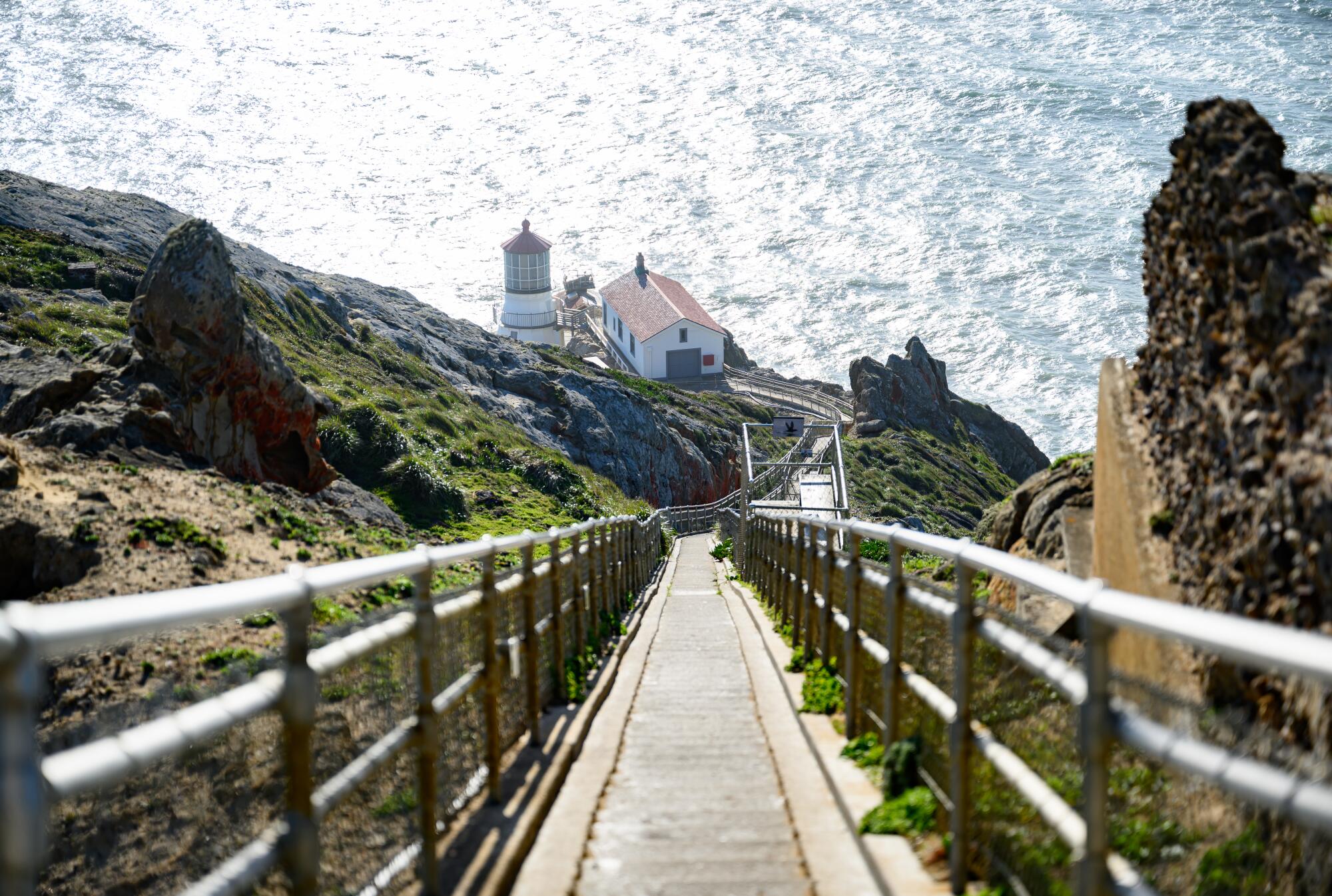 A white lighthouse with a red roof rises above the ocean on a rugged peninsula.