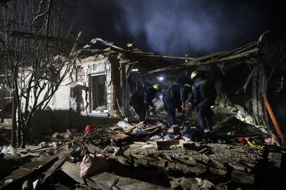 Rescue workers clearing rubble from a destroyed residential building at night.