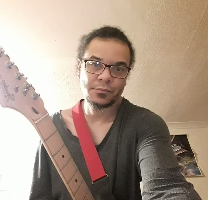 Headshot of Daniel Bannister, holding a guitar.