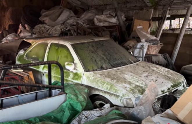 A neglected Ford Escort Cosworth in a cluttered barn.