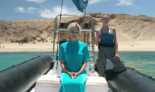 A woman in blue sits on a boat near the coastline