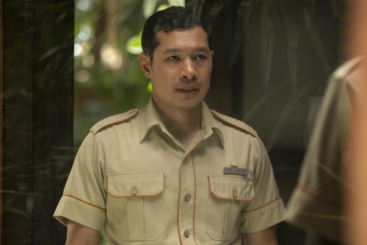 A man in a tan uniform looking through a glass window.