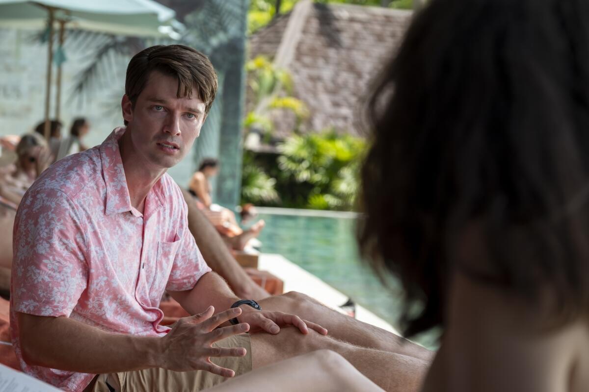 A man in a pink floral shirt and khaki shorts looking at a woman, seen from behind.