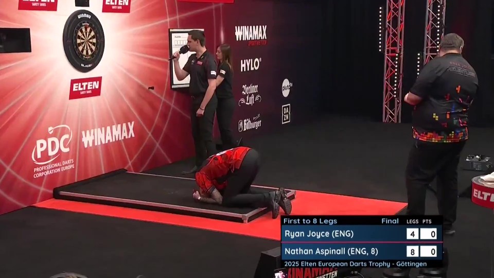 A darts player kneeling on the floor after losing a match.