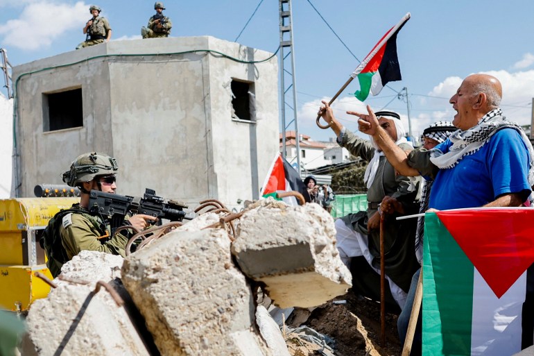 Demonstrators hold Palestinian flags in front of an Israeli soldier 