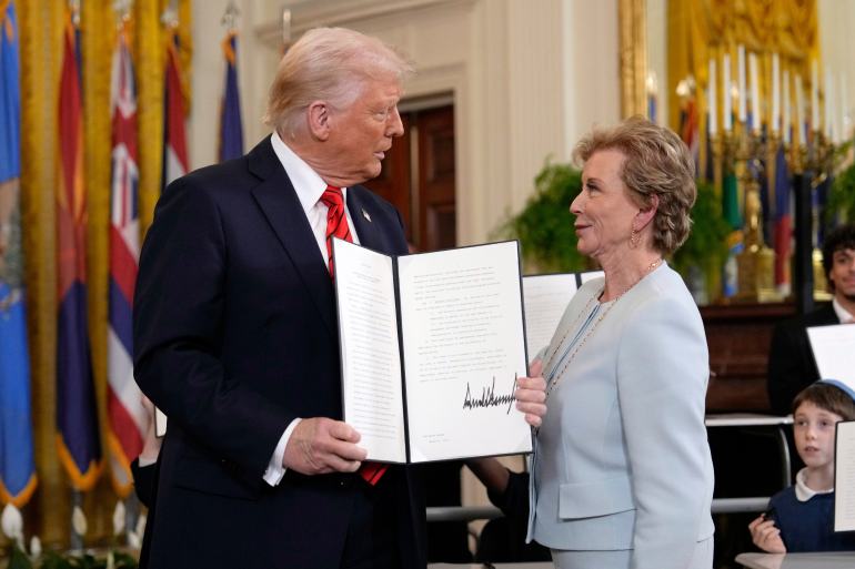 Donald Trump and Linda McMahon in a White House event room, as Trump holds up an executive order to dissolve the Department of Education