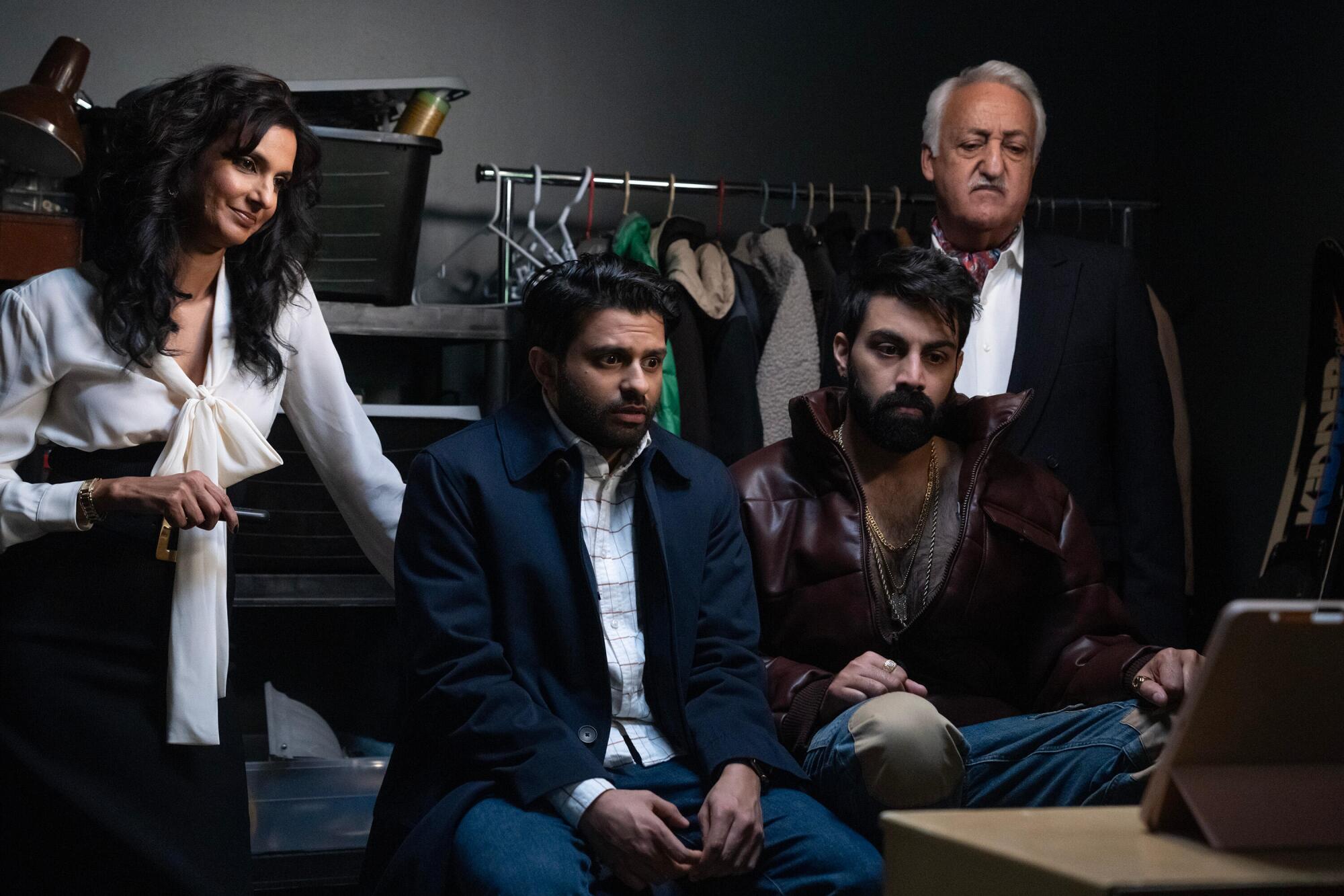 A woman and an older man flank two men sitting in front of a computer tablet on a table.