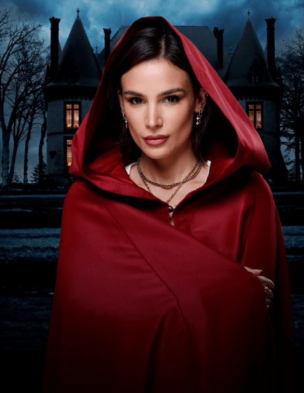 Woman in red hooded cloak in front of a mansion.