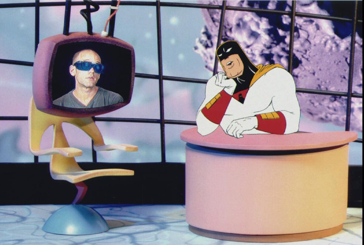 Michael Stipe speaks out of a cartoon TV monitor to Space Ghost, who is seated at a desk like a late-night host