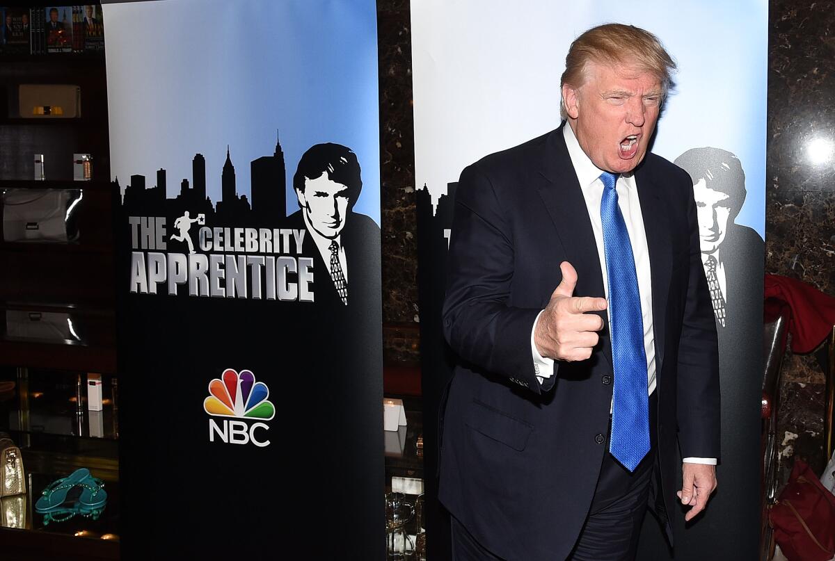 Donald Trump stands next to a banner advertising "The Celebrity Apprentice" in 2015