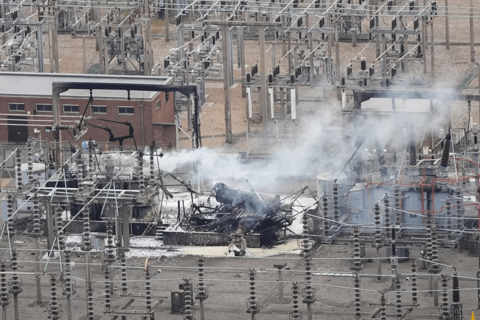 Aerial view of a damaged electrical substation with smoke and fire.