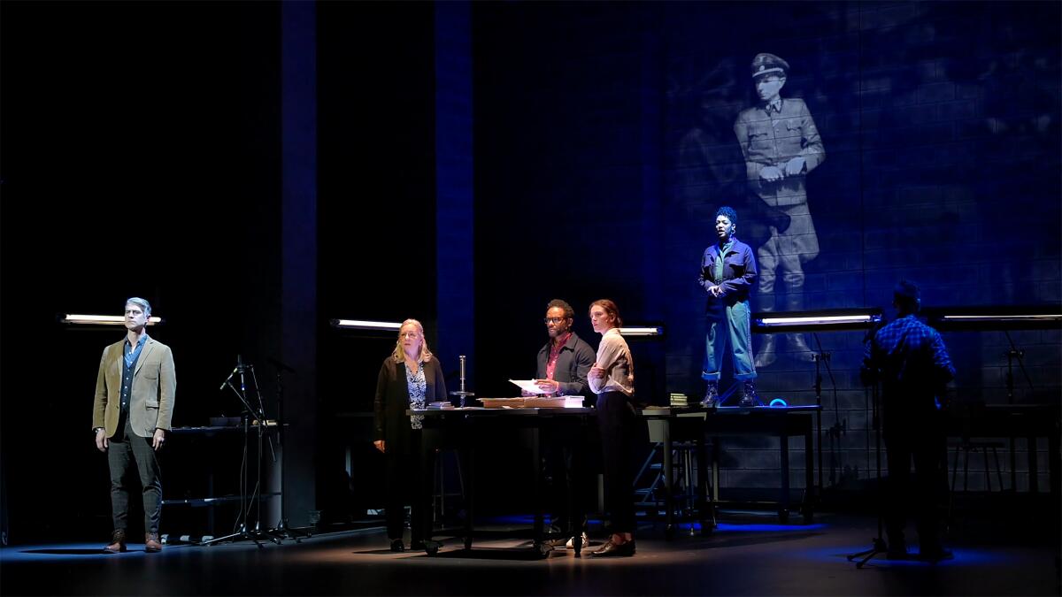 Four cast members on a darkly lit stage.