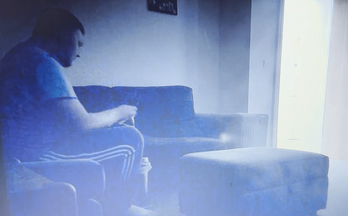 Screenshot of a man sitting on a couch.