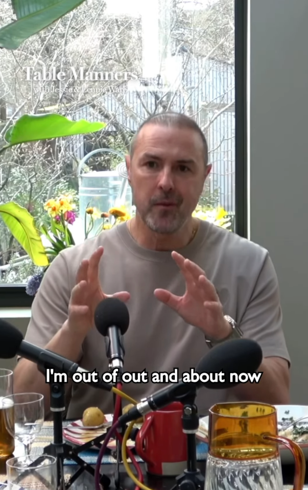 Screenshot of a man sitting at a table with microphones, saying, "I'm out of out and about now."