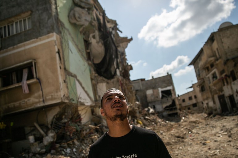 Ismael stands looking up at the camp that was his home, ecompletel surrounded by destruction