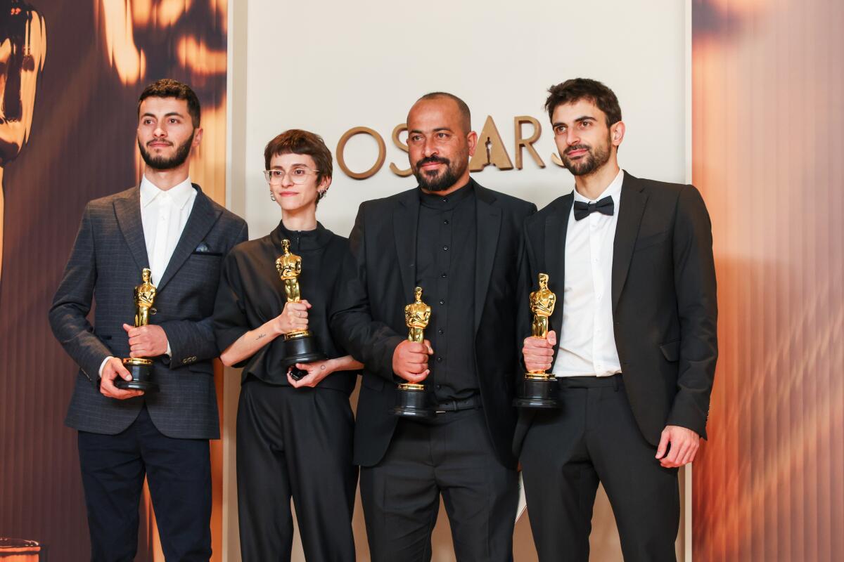 Four people pose with freshly won Oscars.