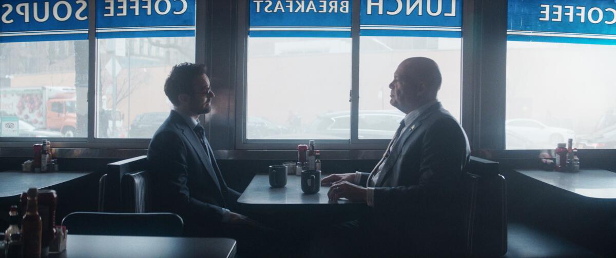 Charlie Cox as Matt Murdock and Vincent D’Onofrio as Wilson Fisk sit across from each other at a table in a diner.