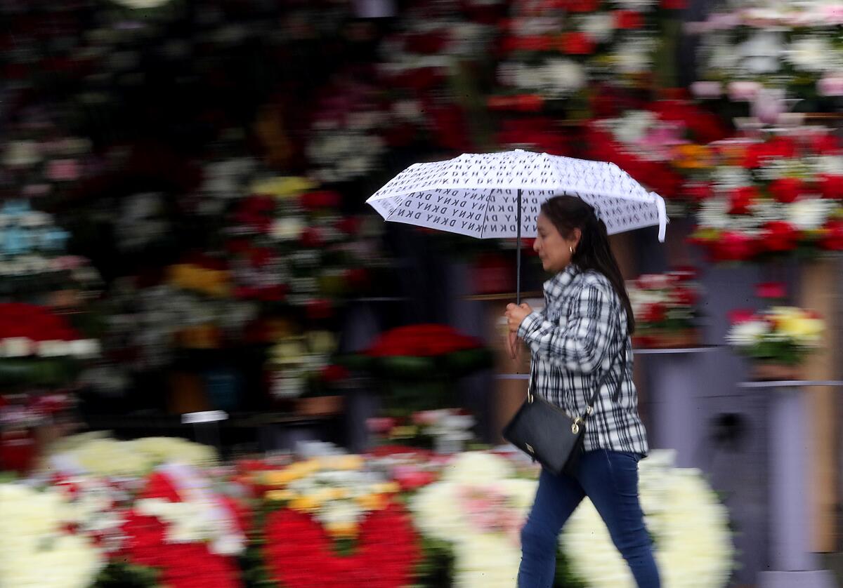 A woman walks past bouquets of flowers while holding an umbrella 