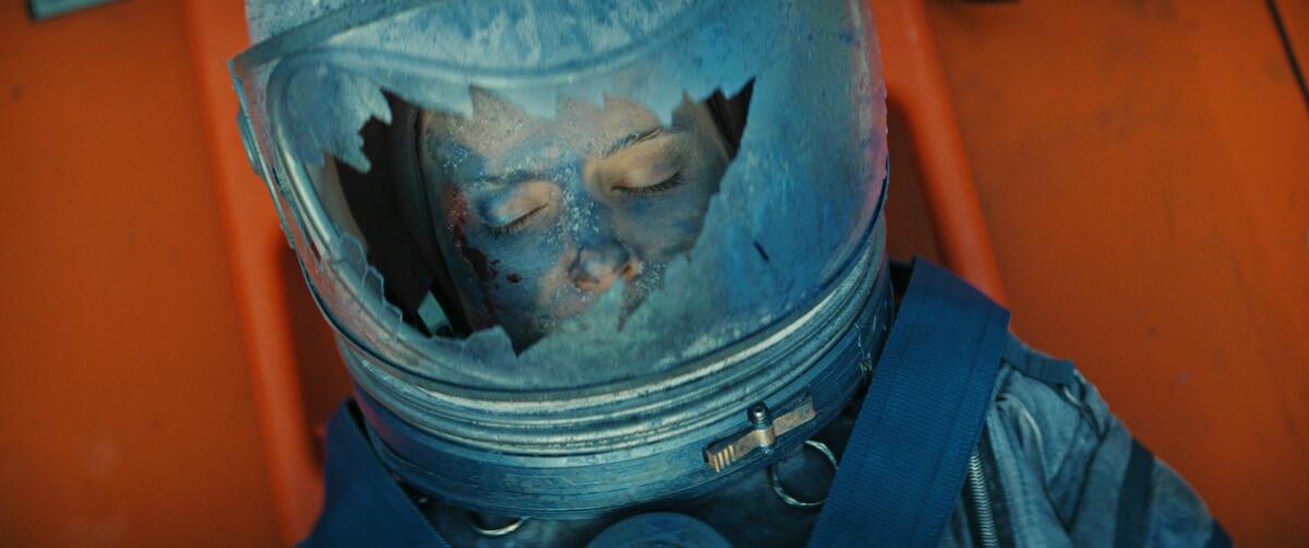 A woman wears a spacesuit with a shattered helmet.