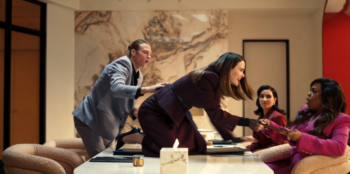 Matthew Noszka tries to hold back Sarah Paulson, who lunges at Niecy Nash and Kim Kardashian from across a conference table. 
