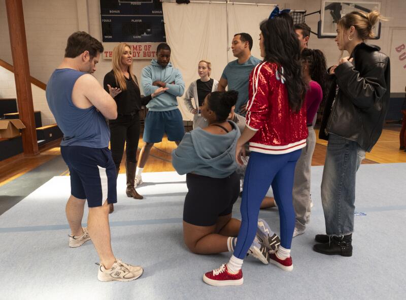 A group of people stand around a woman in black clothing who is gesturing with both hands.