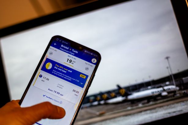 In this photo illustration Ryanair booking app is shown on a mobile phone against a photograph of Ryanair planes displayed on a computer screen as the company expects to take more passenger next year - November 3, 2025.