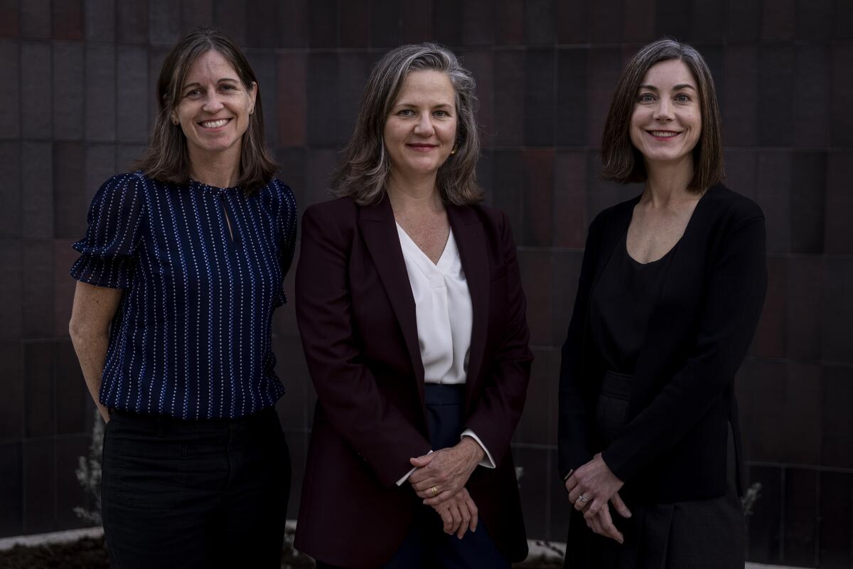 Liz MacLean stands with her hands behind her back while Leslie Denk and Emily Talbot stand with hands folded.