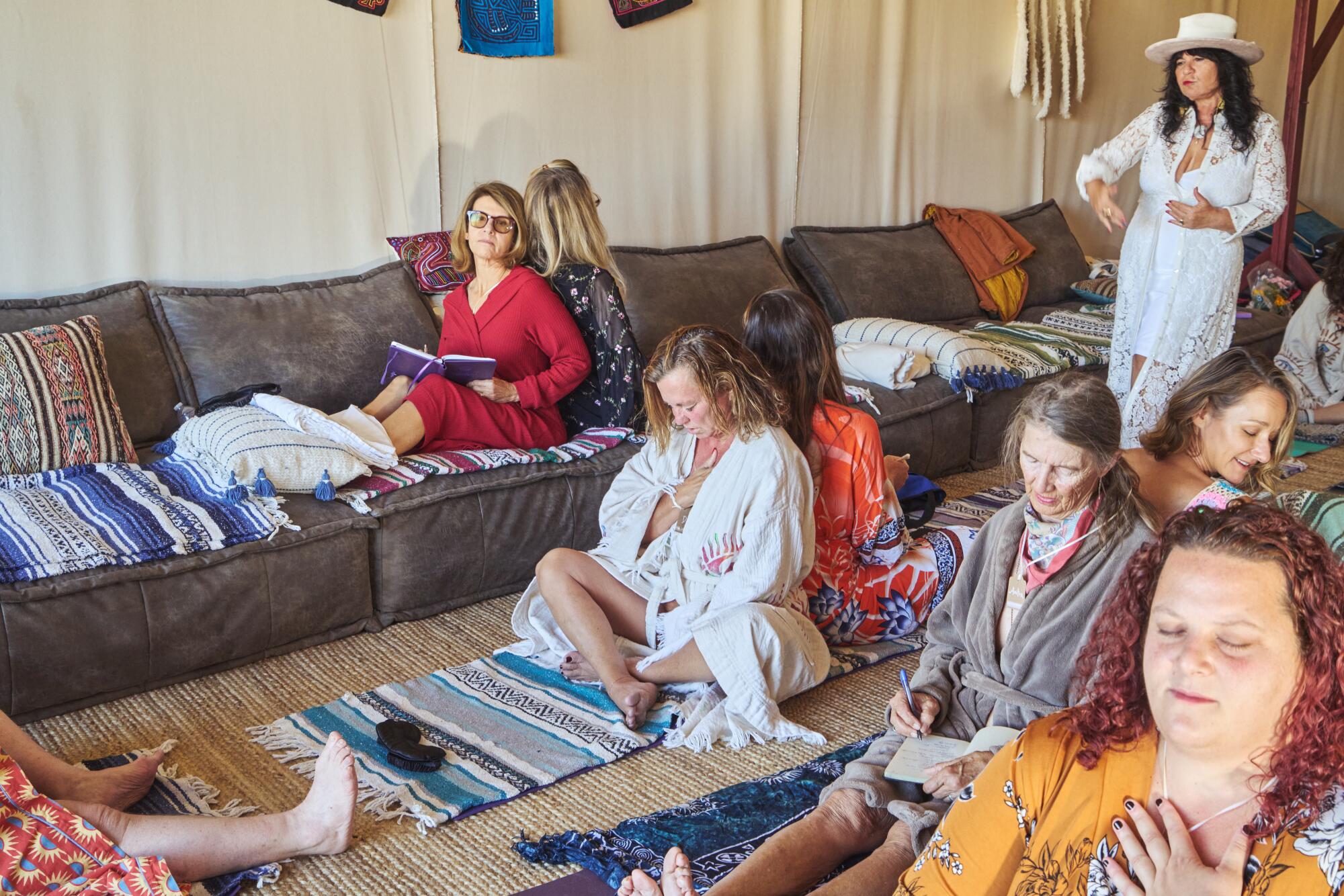 Women sit on the floor in pairs, back to back, journaling. 