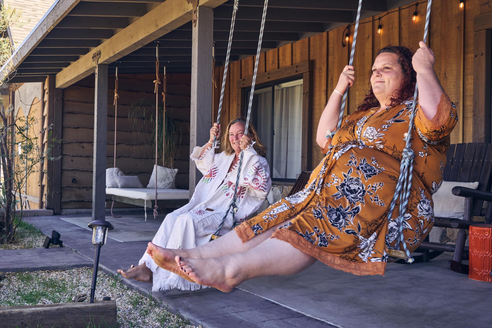 Two women on swings on a porch.