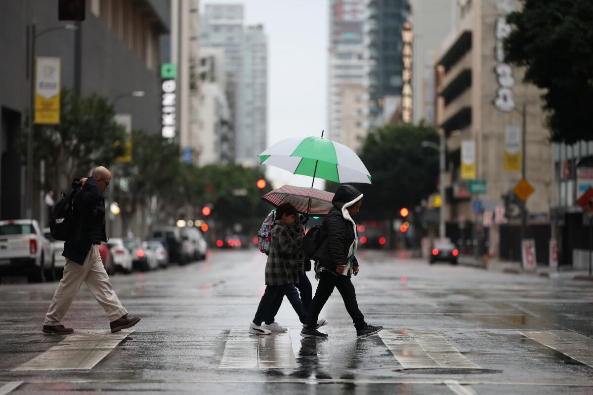 Pedestrians cross the street in downtown Los Angeles under light rain on Friday.