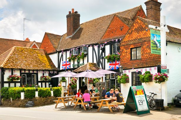 People sitting outside in summer enjoying food and drinks at the White Horse Inn, a traditional 15th-century pub in the picturesque village of Shere in Surrey, England, UK. 