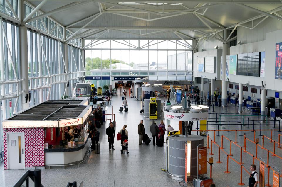 Interior of Bristol Airport showing various people, a Moneycorp currency exchange kiosk, and check-in desks.
