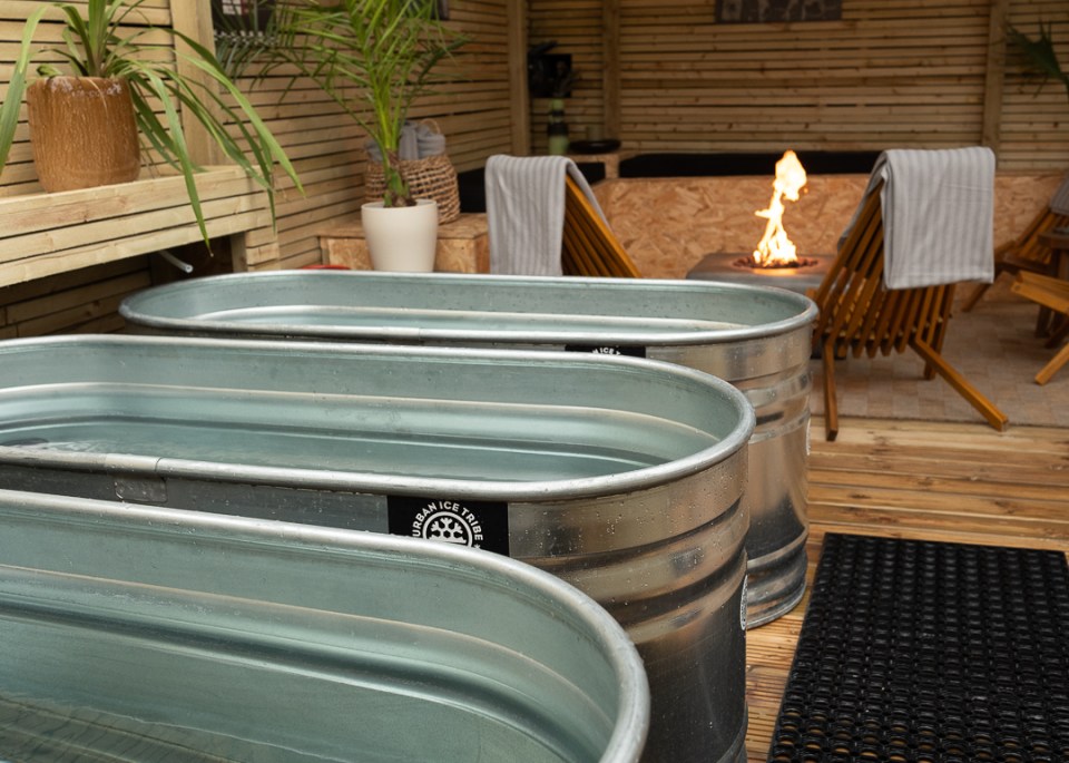 Ice bath tubs on a wooden deck with a fire pit in the background.