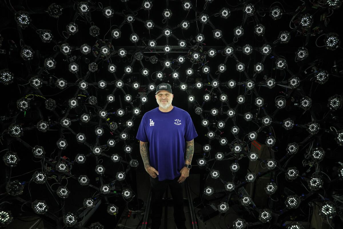 A man in a blue shirt stands in front of dozens of lights.