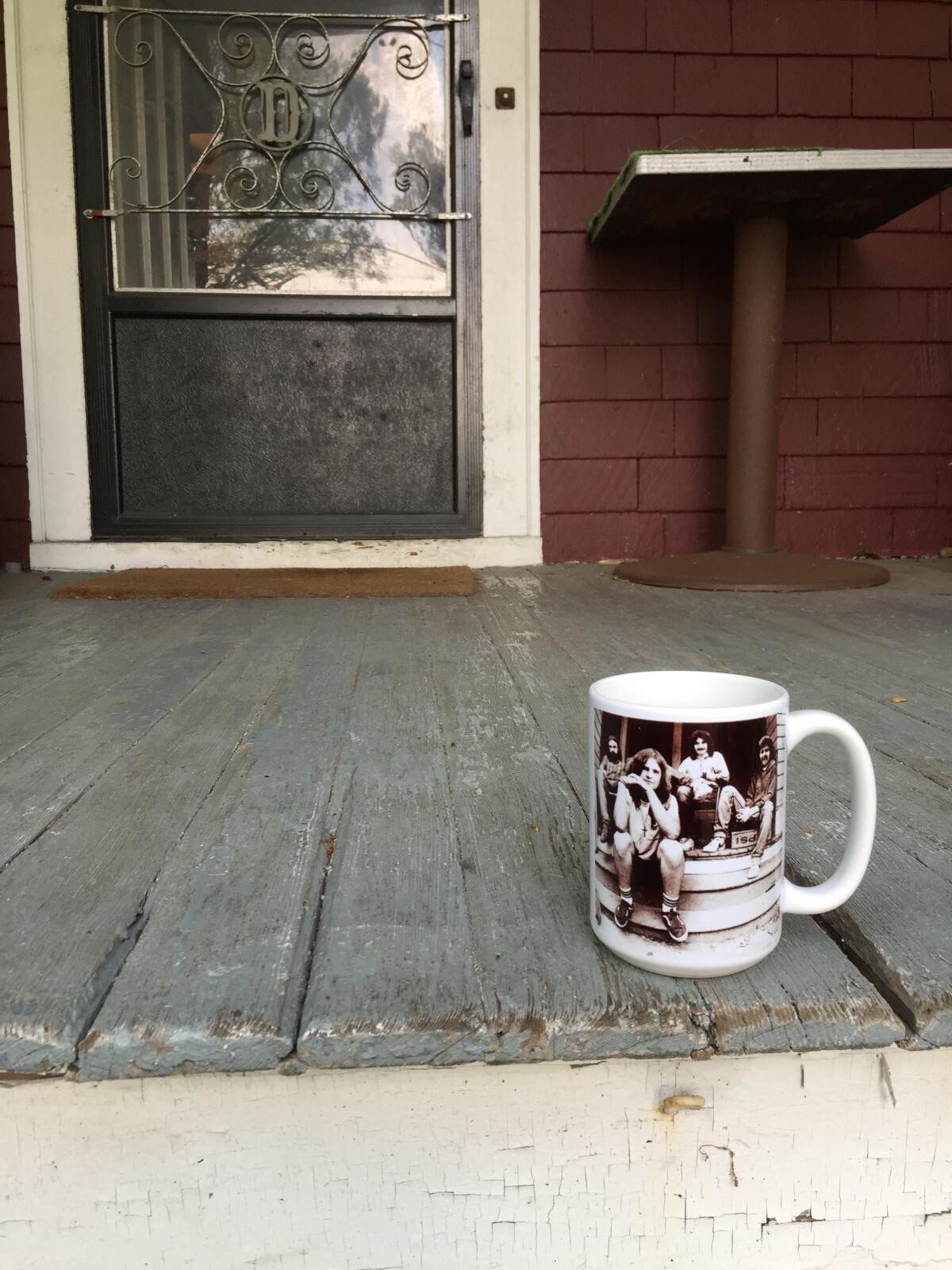 A coffee mug with a band photo on it sits on a porch.