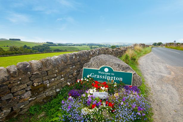 Welcome to Grassington sign in the road in front of a small flower garden
