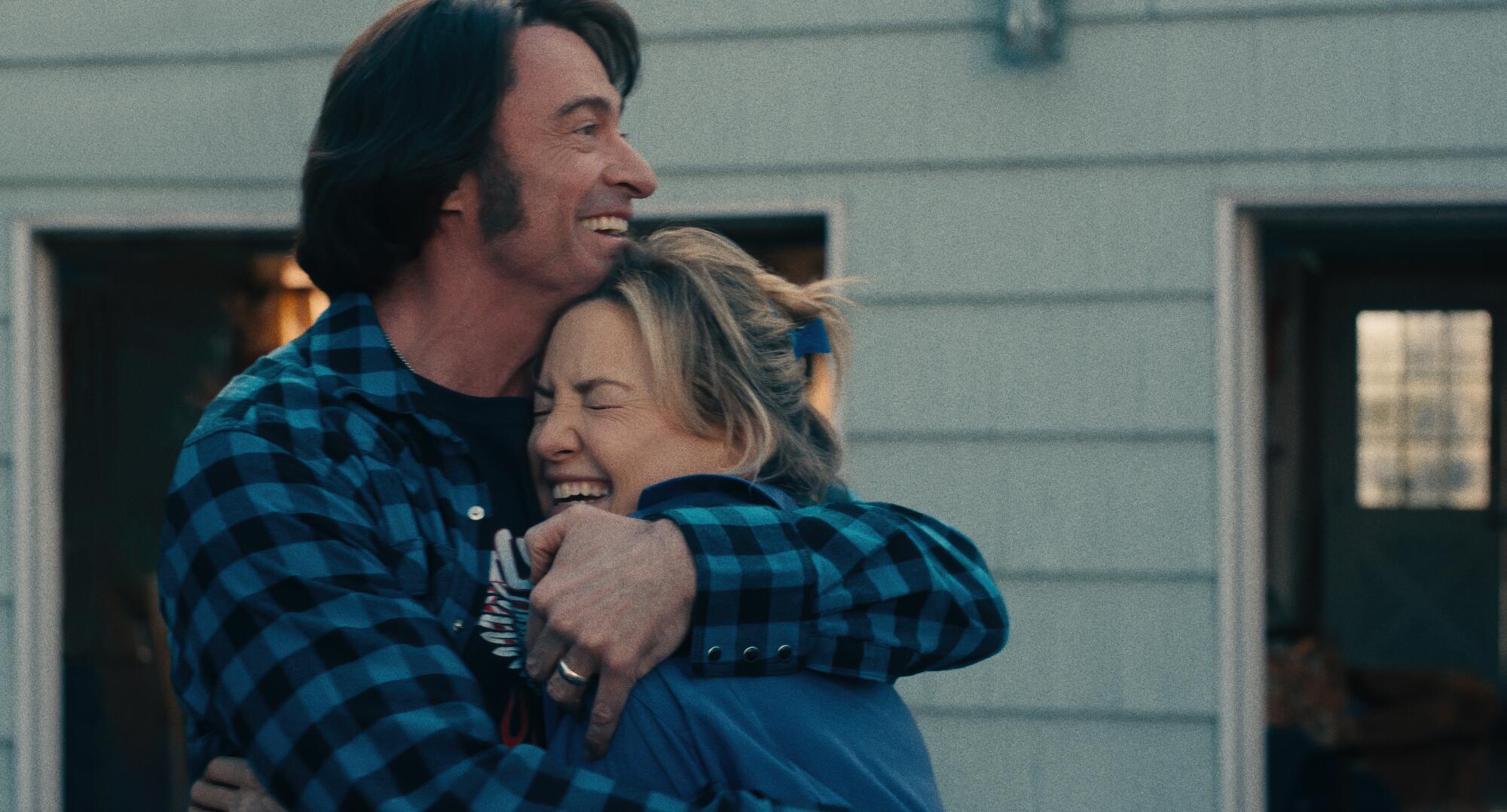 A woman and a man hug in front of their house.