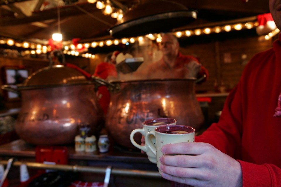 Hands holding two mugs of mulled wine at a Christmas market.
