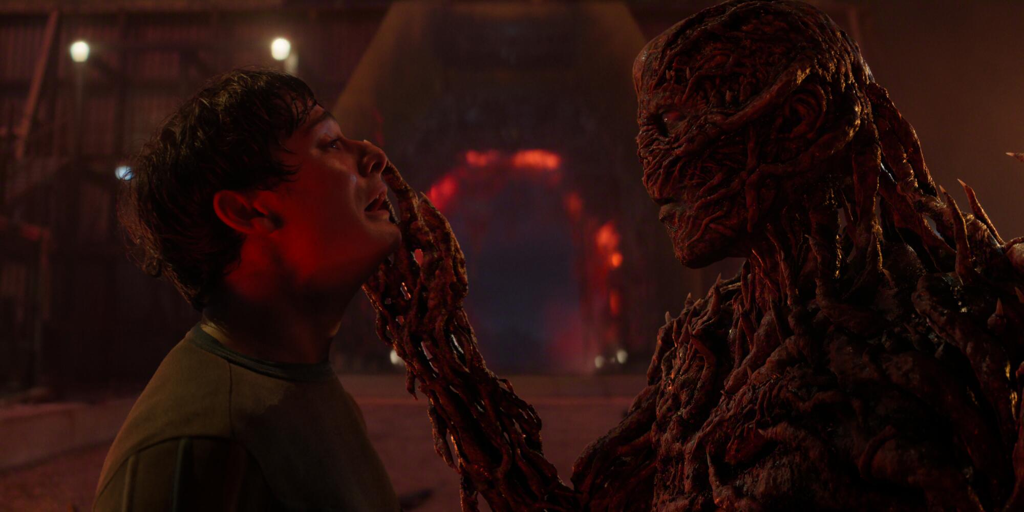 A still photo from "Stranger Things" of a monster holding the face of a scared young man