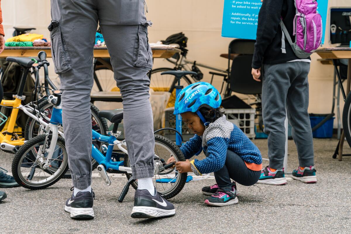 A small child in a blue bike helmet squats down to work on a blue bicycle.