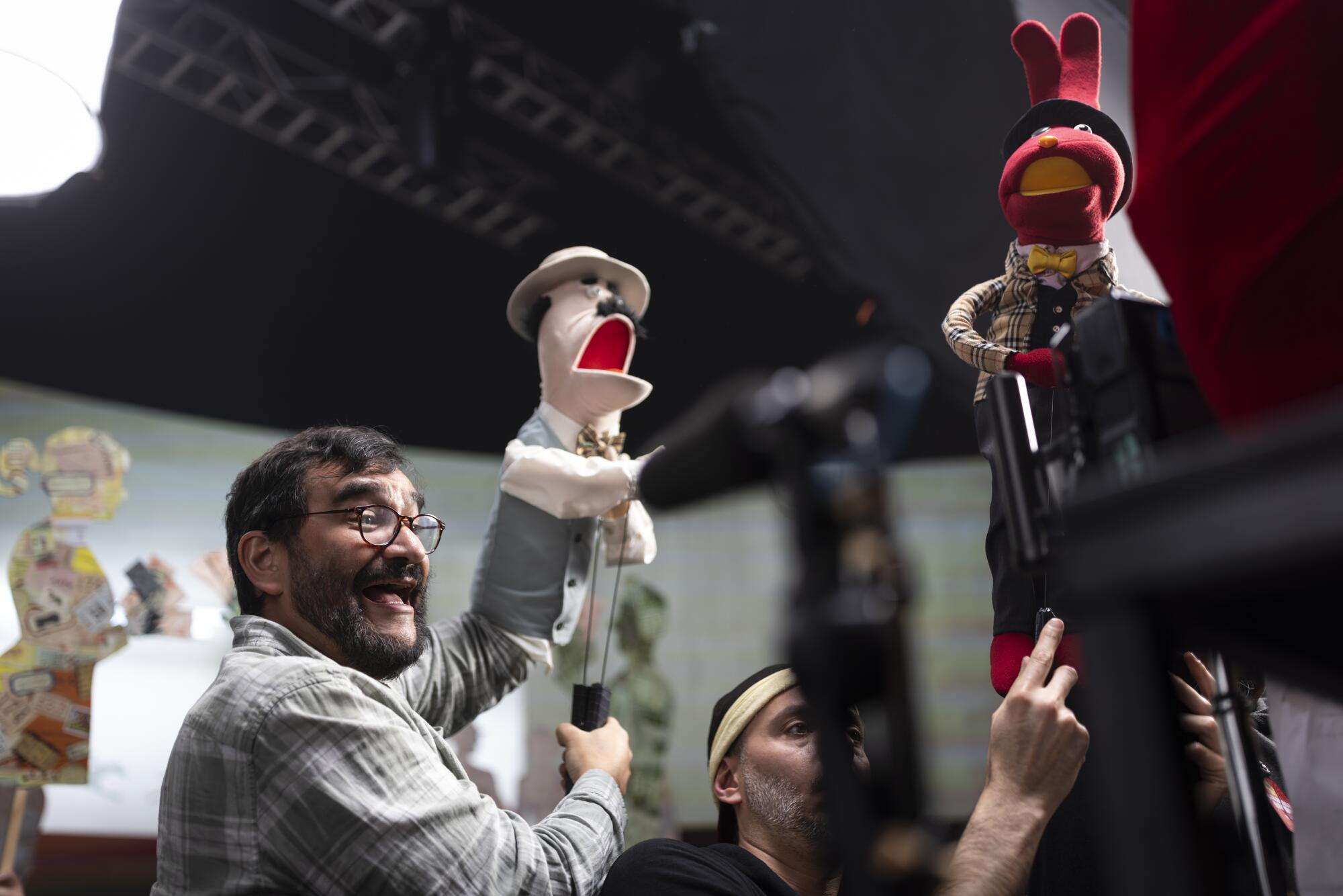 Two men holding and voicing puppets.