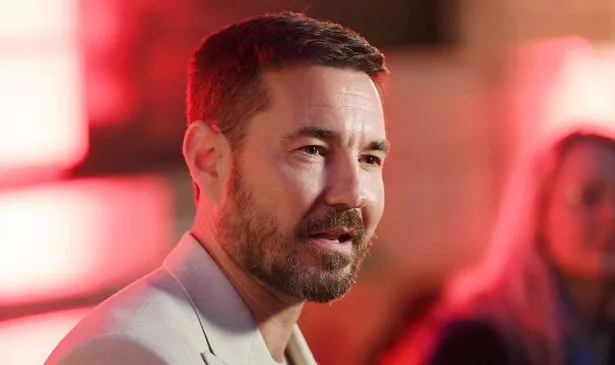 A man in a suit stands in a red room