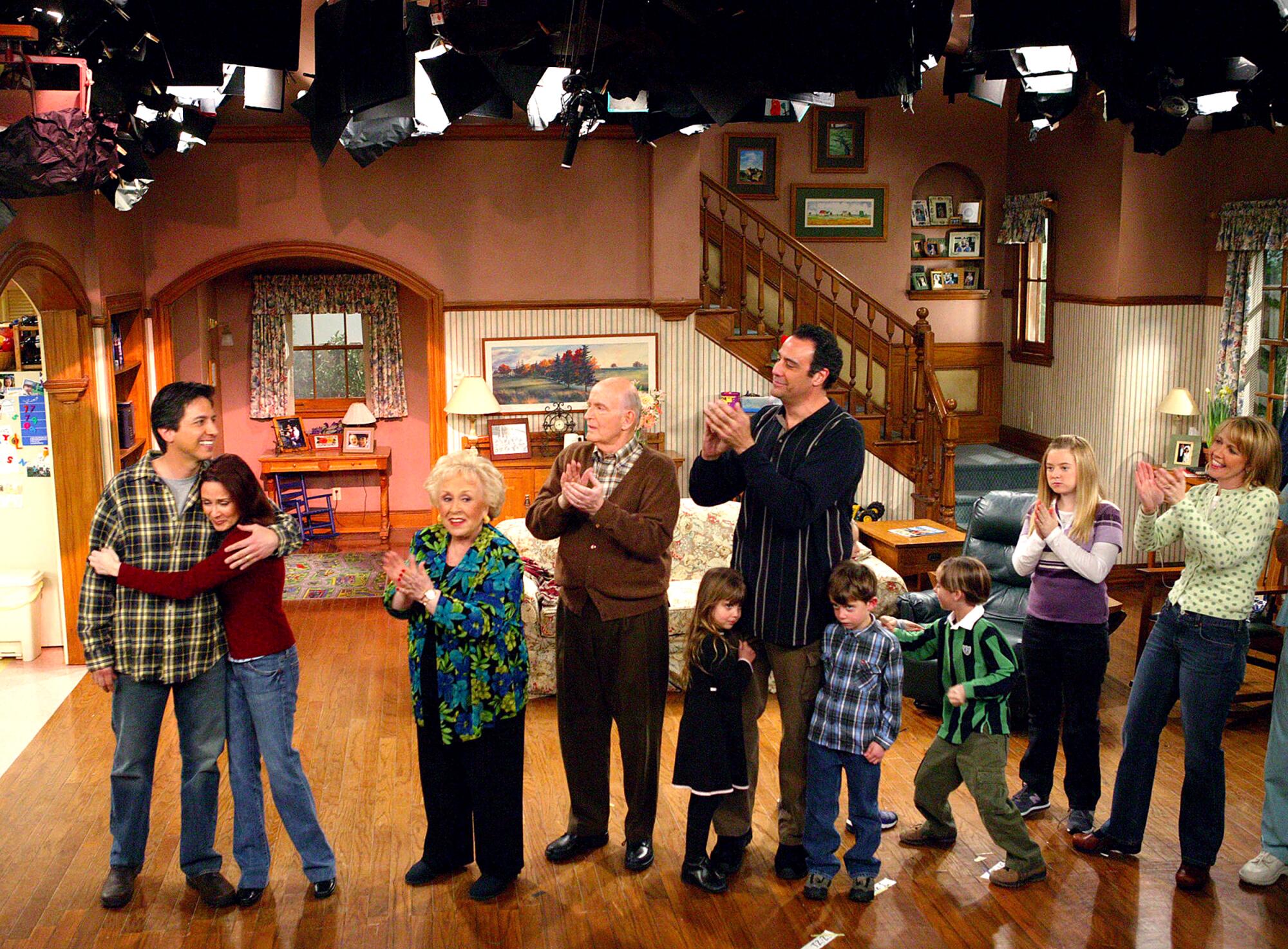 A group of 10 people clapping and standing on the set of a television show.