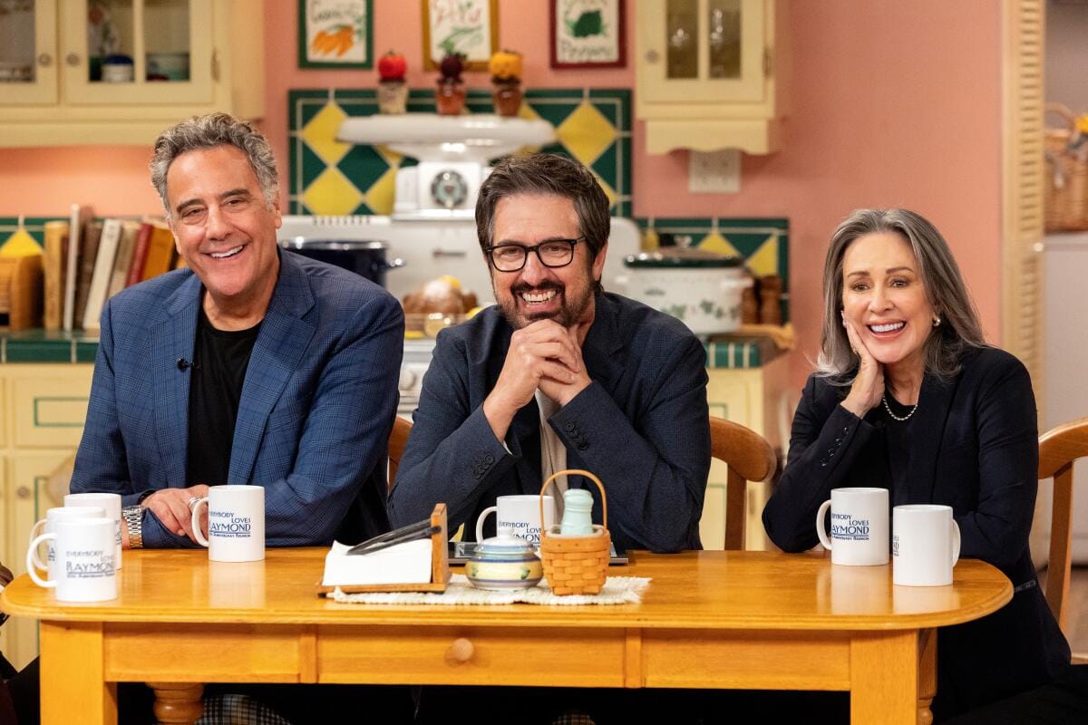 Two men and a woman smiling and sitting at a small table with coffee cups in front of them.