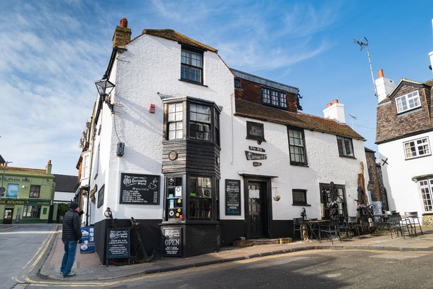 A man stands outside the quaint Old Curiostiy Shop in Broadstairs, Kent on a bright winter day with blue sky