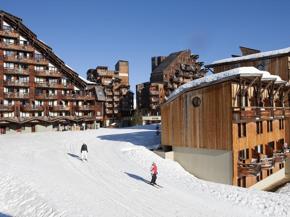 Skiers on a snowy slope in front of wooden ski resort buildings.