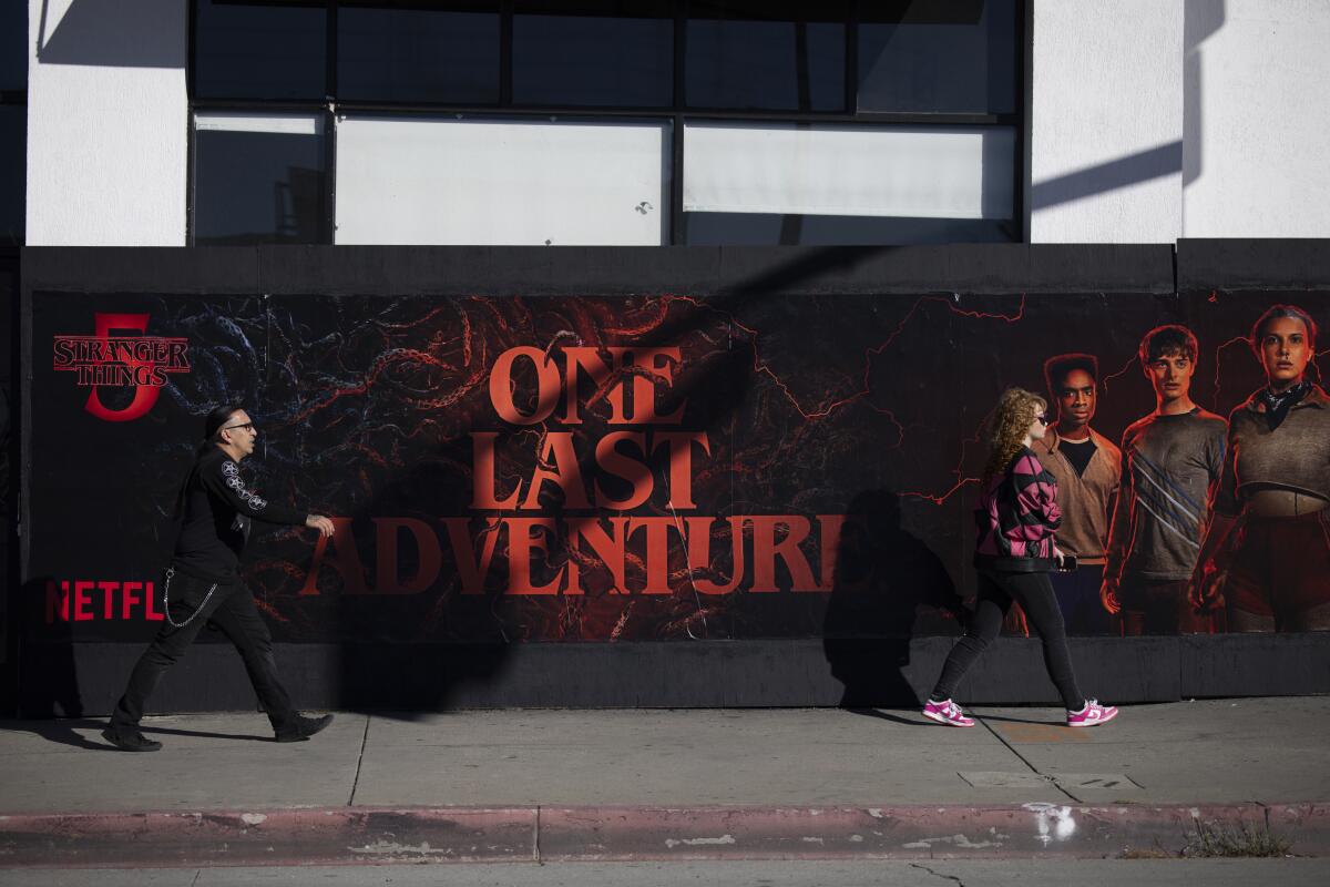 Omar Chavez, 42, left, and Jenna Chavez, 28, right, from West Hollywood walk past a poster.